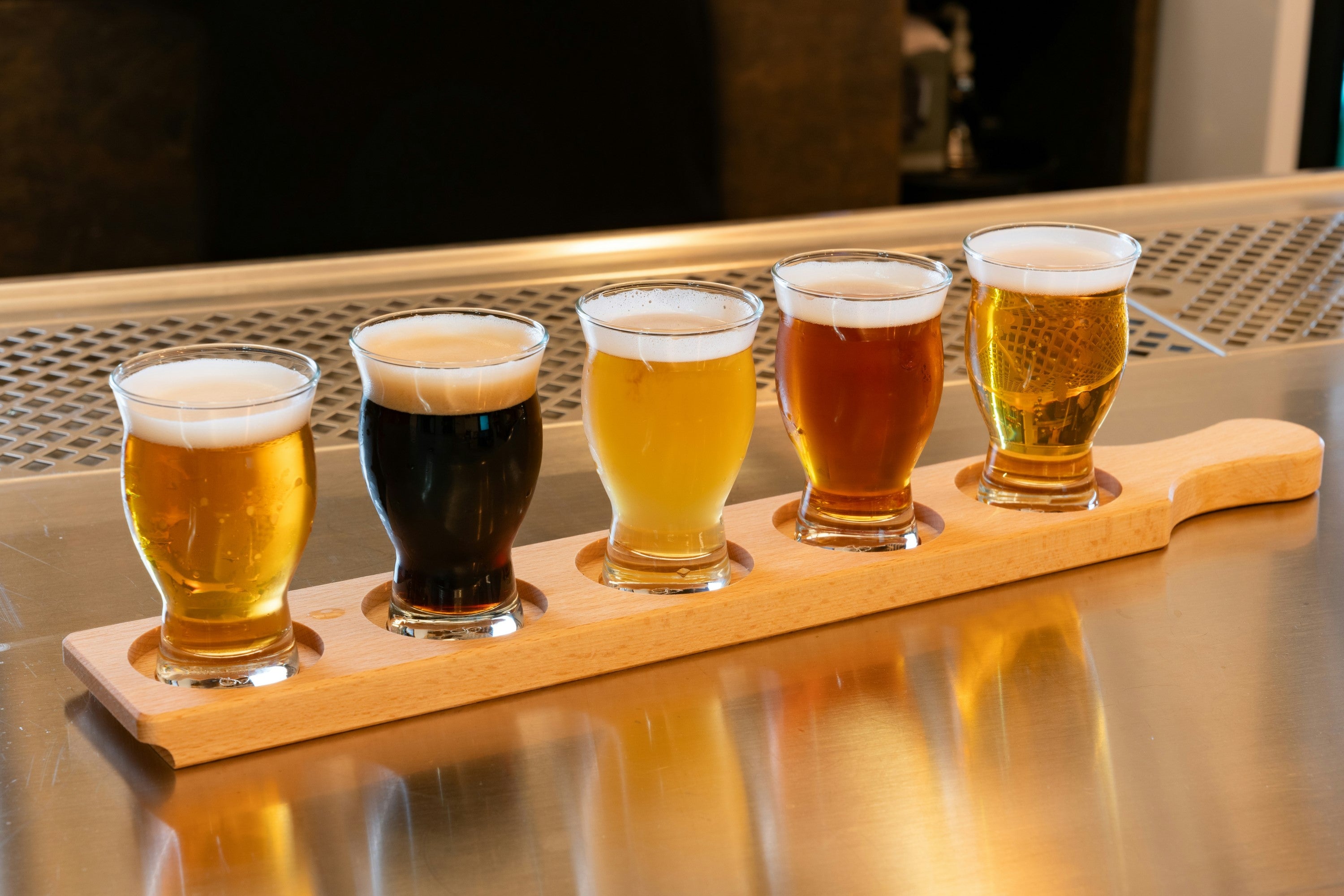 A row of beer glasses on a wooden tray, showcasing grain-based drinks that can trigger reactions in individuals sensitive to gluten or alcohol.