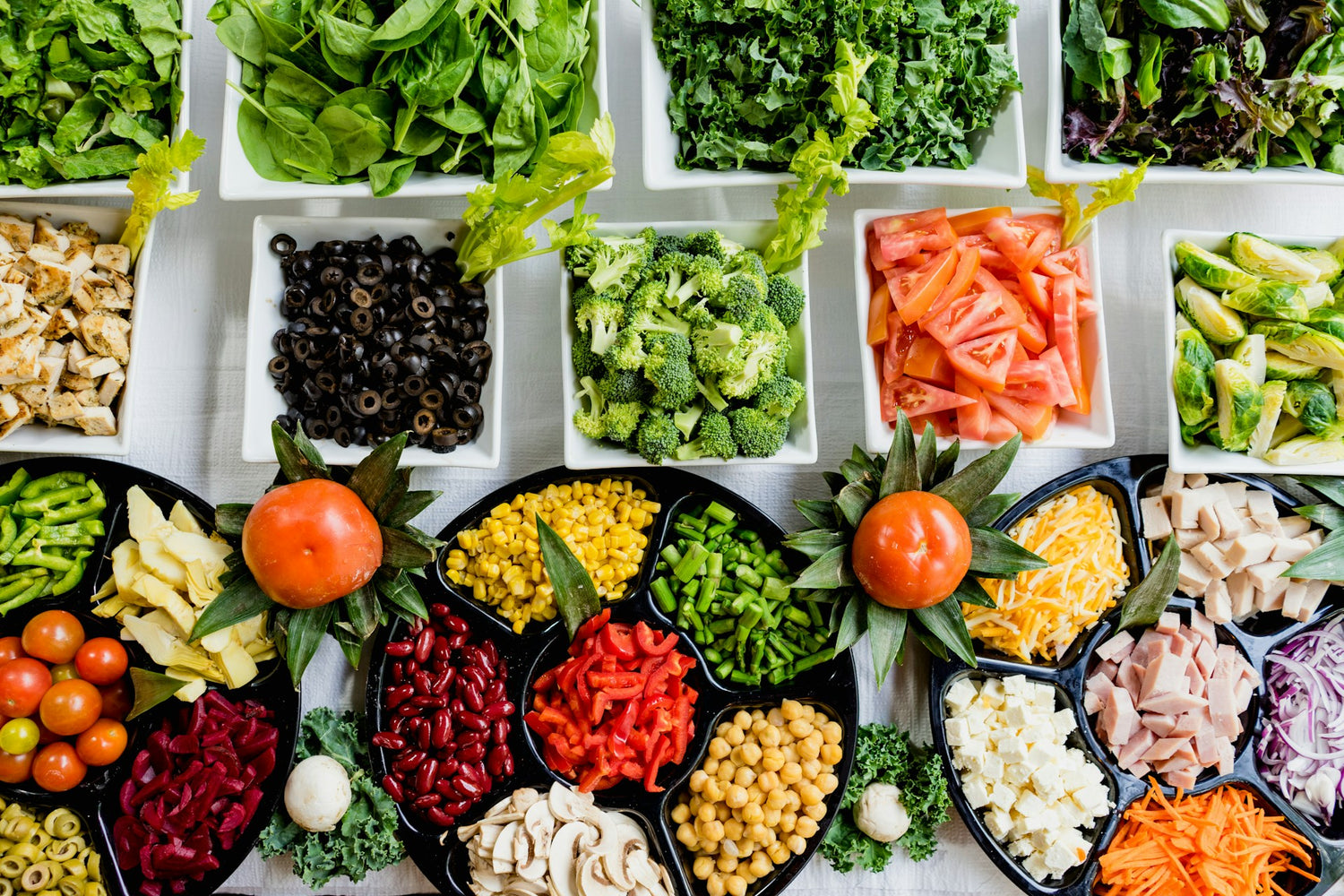 A colourful assortment of fresh salad ingredients, including spinach, kale, tomatoes, broccoli, olives, chickpeas, and shredded cheese, demonstrating yeast-free meal preparation ideas.