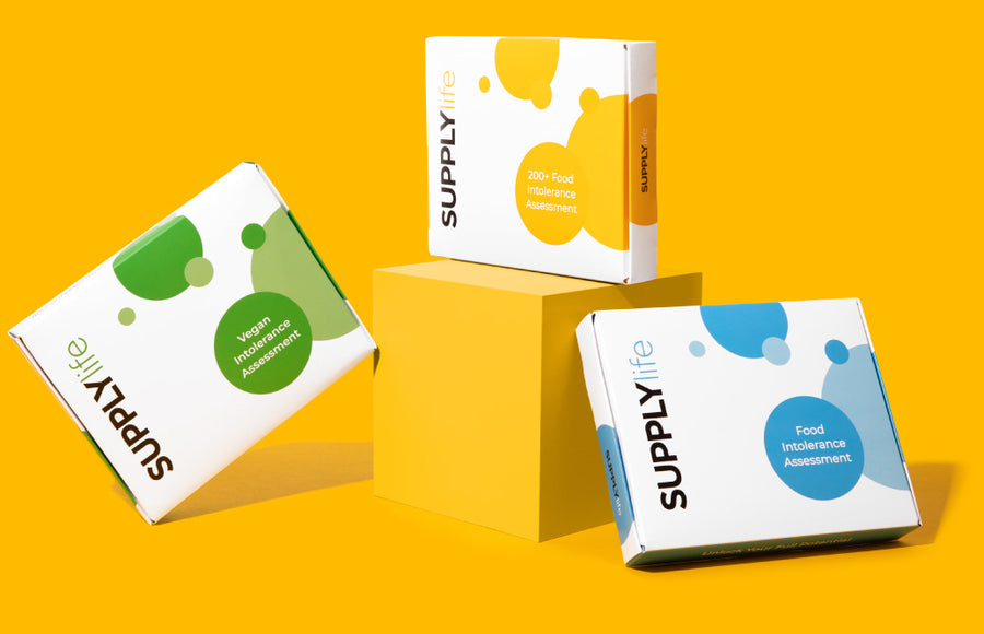 Three food intolerance assessment kits displayed against a vibrant yellow background. The kits are in white boxes with colorful designs: green for 'Intolerance Assessment', yellow for '200+ Food Intolerance Assessment', and blue for 'Food Intolerance Assessment'