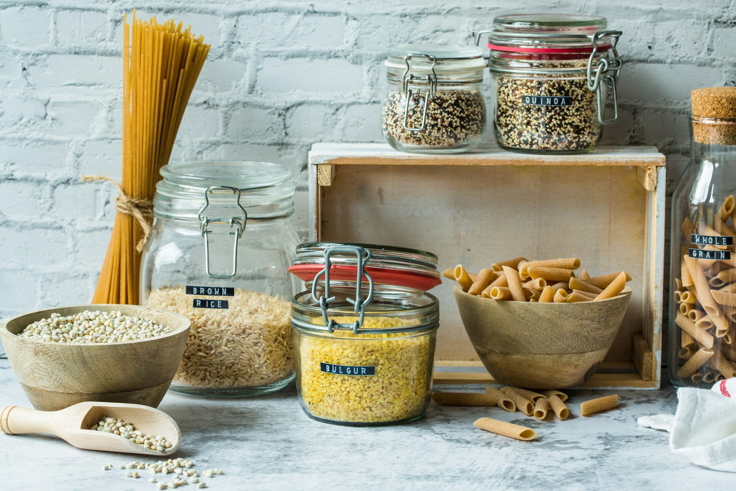 A selection of dry whole grains and pasta, including brown rice, quinoa, bulgur, and whole grain penne, displayed in glass jars and wooden bowls, showcasing naturally yeast-free options for those with yeast intolerance