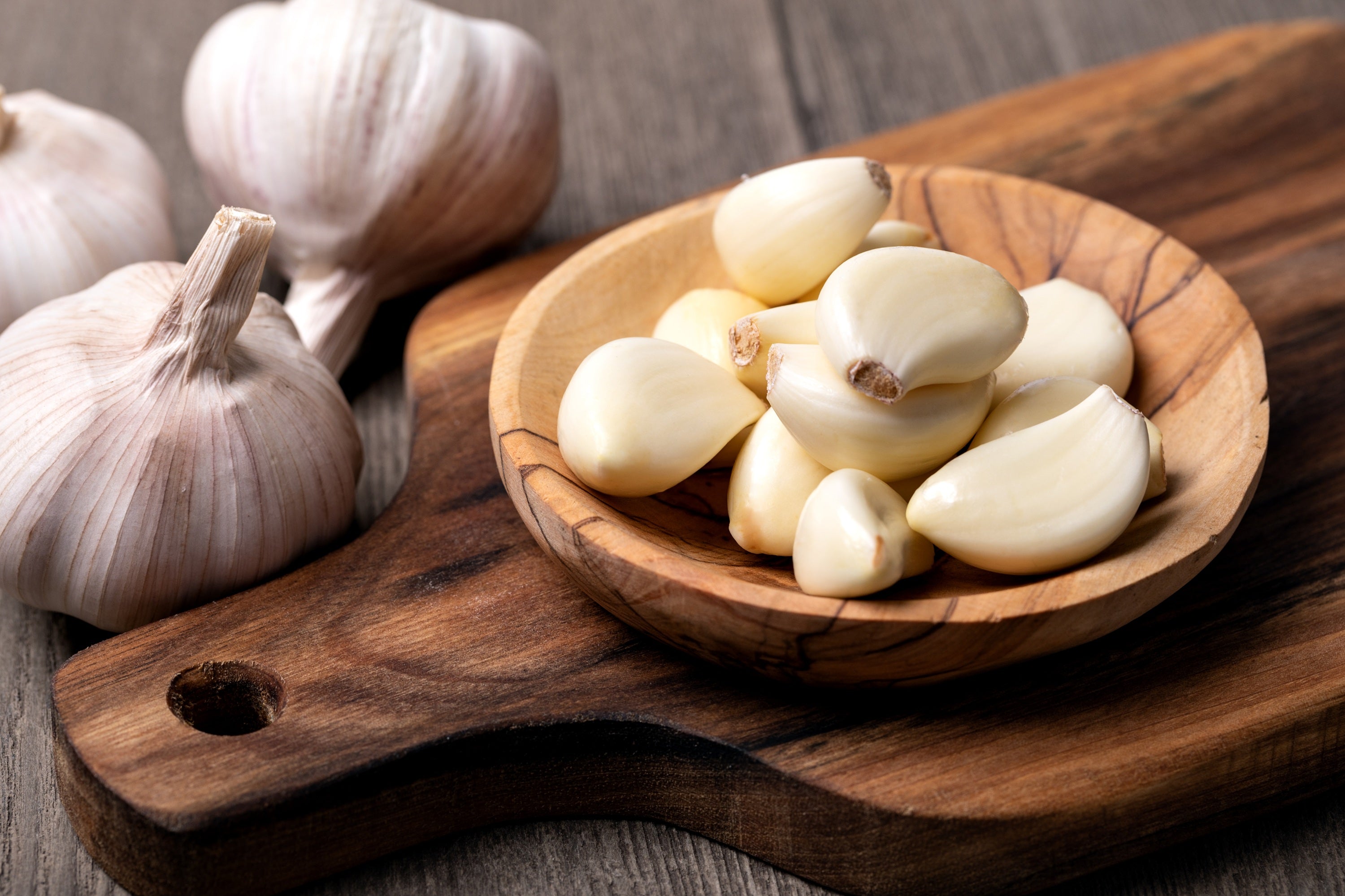 Fresh garlic cloves scattered on a wooden cutting board, showcasing their natural texture and color.