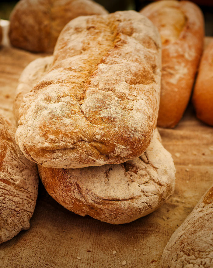 Close-up of rustic, flour-dusted loaves of bread stacked on a wooden surface, a common source of yeast that may trigger intolerance symptoms.