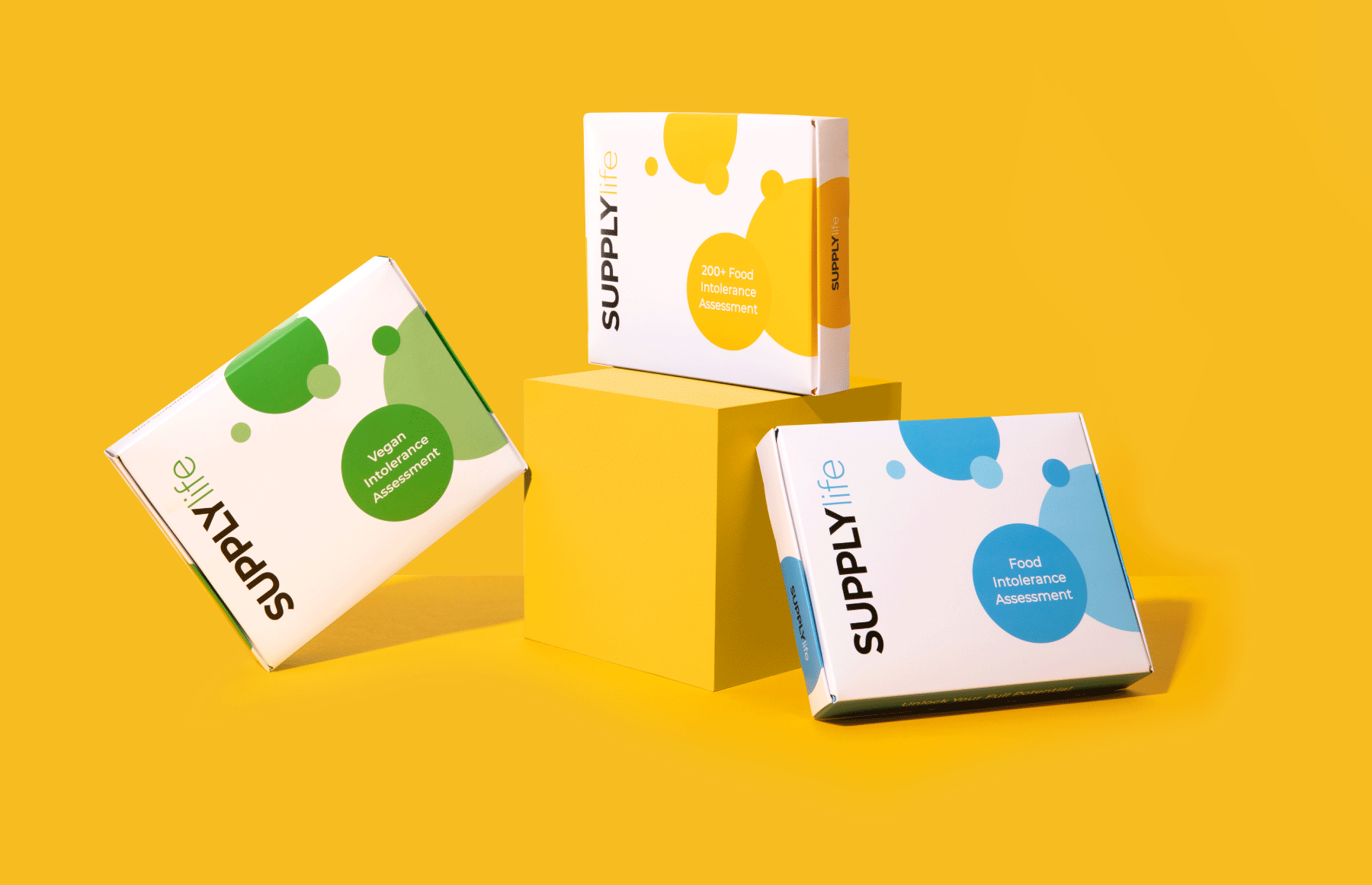 Three food intolerance assessment kits displayed against a vibrant yellow background. The kits are in white boxes with colorful designs: green for 'Intolerance Assessment', yellow for '200+ Food Intolerance Assessment', and blue for 'Food Intolerance Assessment'.